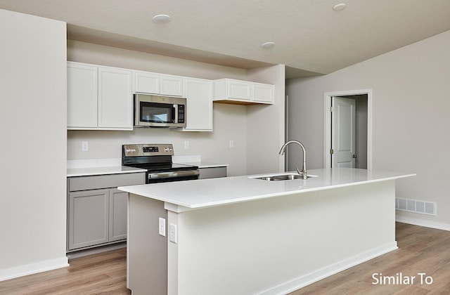 kitchen featuring sink, white cabinets, a kitchen island with sink, stainless steel appliances, and light wood-type flooring