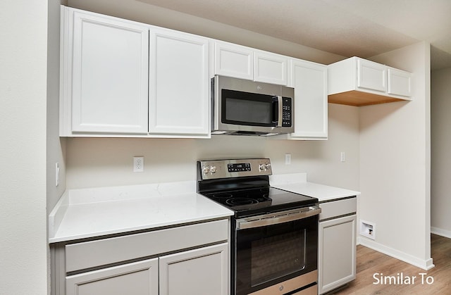 kitchen with appliances with stainless steel finishes, light hardwood / wood-style flooring, and white cabinets