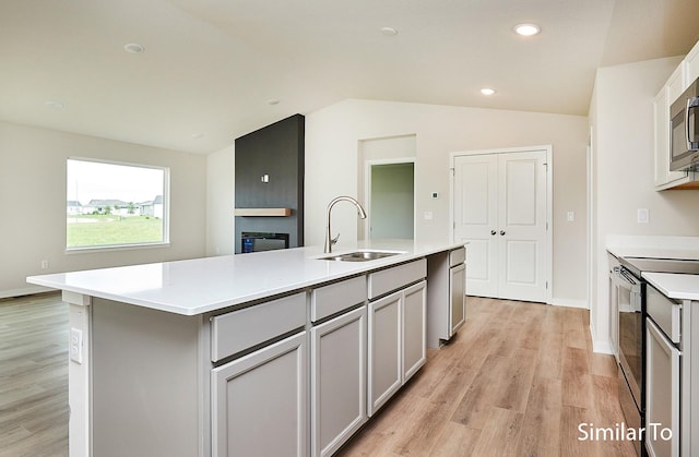 kitchen featuring sink, stainless steel range with electric stovetop, gray cabinetry, a center island with sink, and vaulted ceiling