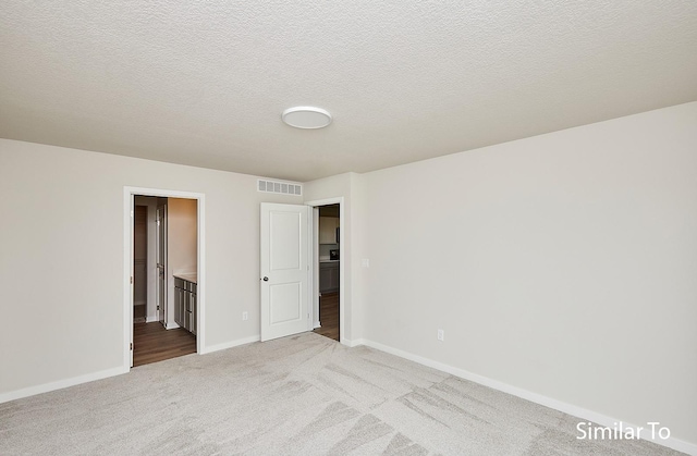 unfurnished bedroom featuring light colored carpet, ensuite bathroom, and a textured ceiling