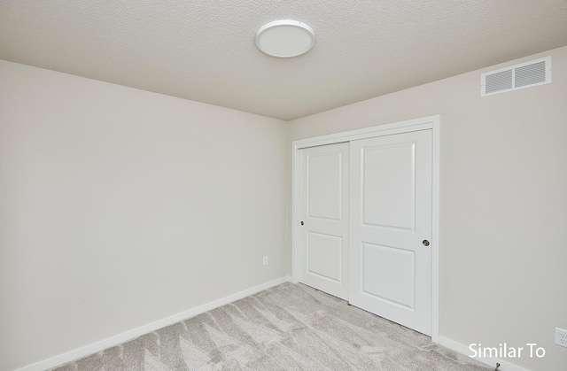 unfurnished bedroom with light carpet, a textured ceiling, and a closet