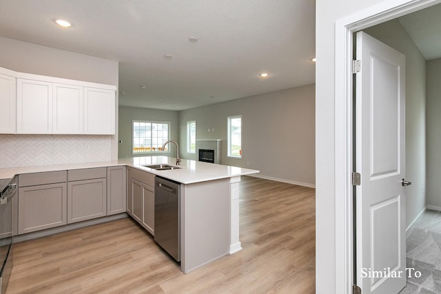 kitchen with dishwasher, sink, decorative backsplash, light wood-type flooring, and kitchen peninsula