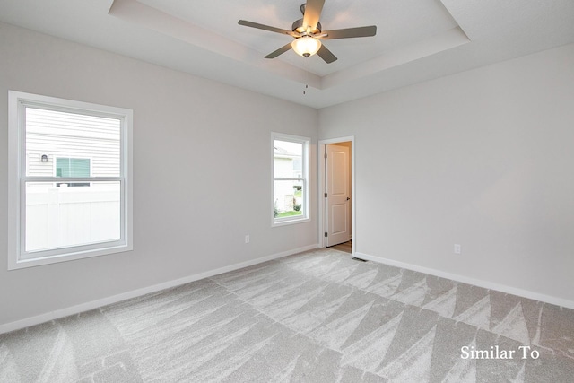 unfurnished room with light carpet, a raised ceiling, ceiling fan, and a healthy amount of sunlight