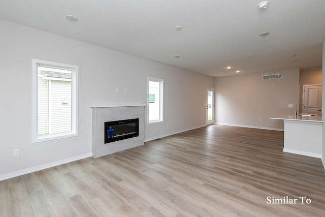 unfurnished living room featuring sink, light hardwood / wood-style flooring, a wealth of natural light, and a tiled fireplace