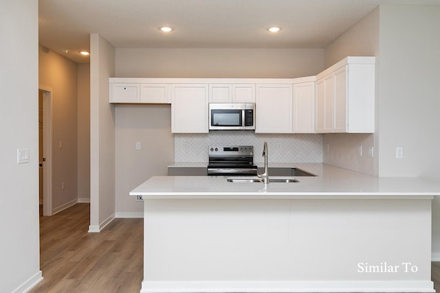 kitchen featuring sink, kitchen peninsula, decorative backsplash, white cabinets, and appliances with stainless steel finishes