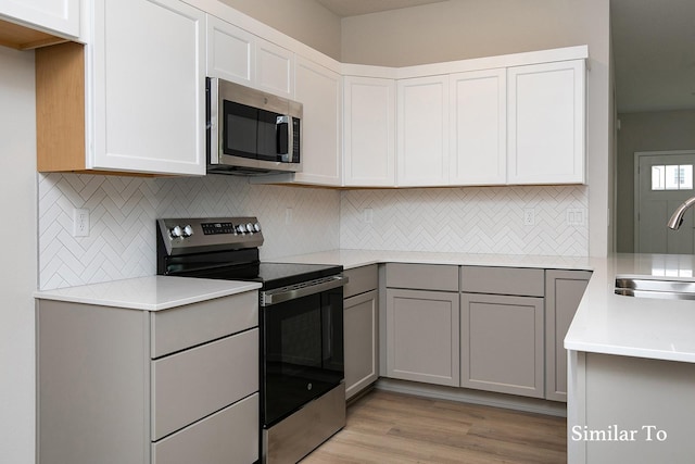 kitchen with gray cabinetry, sink, tasteful backsplash, appliances with stainless steel finishes, and light wood-type flooring