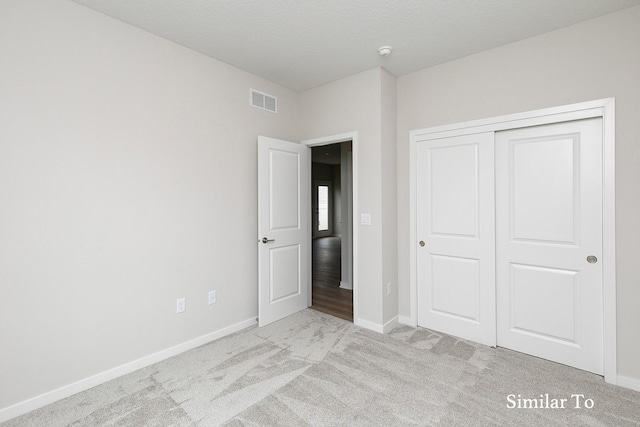 unfurnished bedroom featuring a textured ceiling, light carpet, and a closet