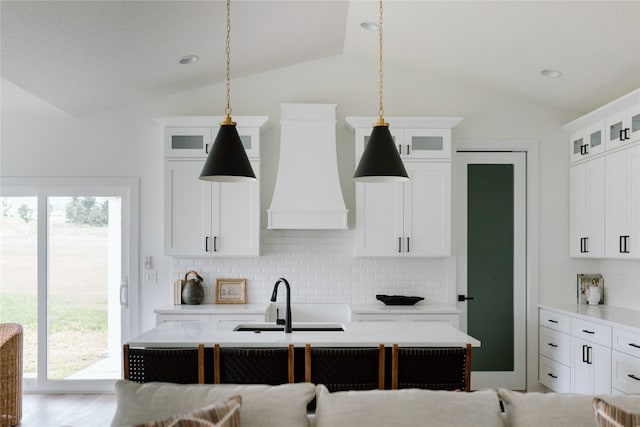 kitchen featuring custom exhaust hood, vaulted ceiling, sink, pendant lighting, and white cabinetry