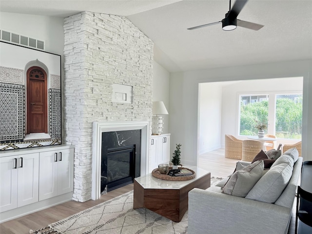 living room with a high end fireplace, a textured ceiling, vaulted ceiling, ceiling fan, and light hardwood / wood-style flooring