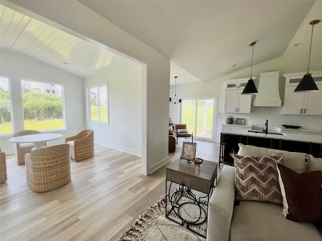 living room with light hardwood / wood-style floors, vaulted ceiling, a notable chandelier, and sink