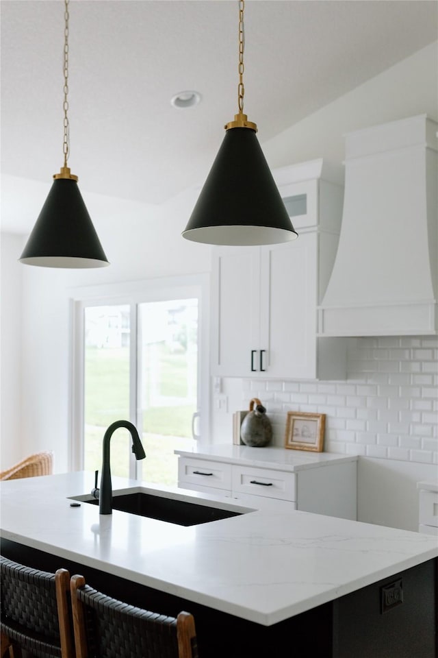 kitchen featuring white cabinets, custom range hood, pendant lighting, and sink