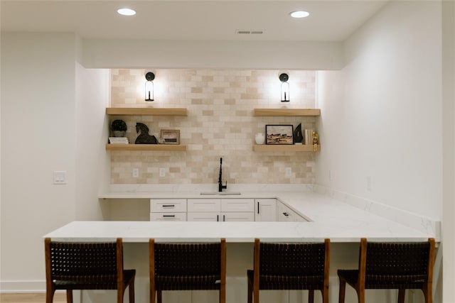 bar with light stone countertops, tasteful backsplash, white cabinetry, and sink