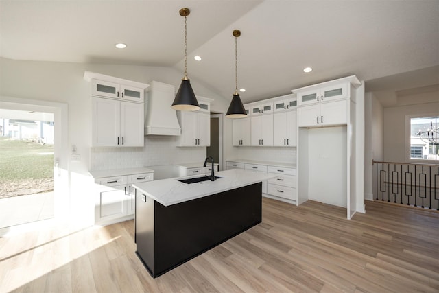 kitchen with white cabinets, a center island with sink, premium range hood, and lofted ceiling