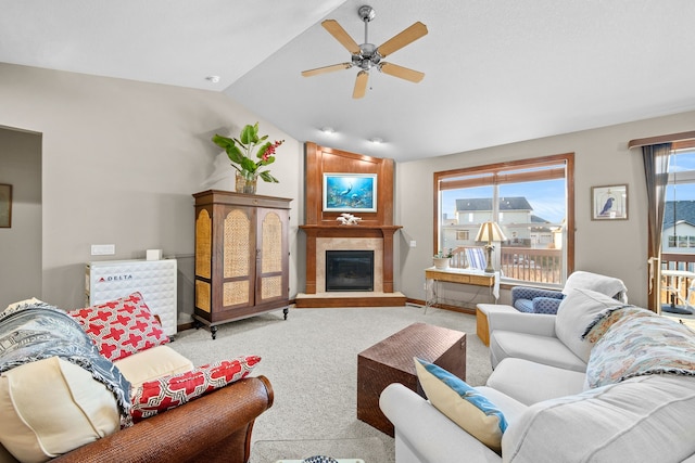 carpeted living room with ceiling fan, a large fireplace, and vaulted ceiling