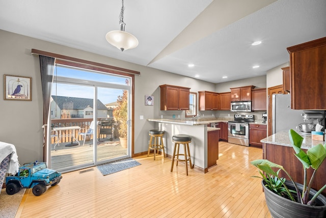 kitchen featuring light hardwood / wood-style floors, vaulted ceiling, decorative light fixtures, a breakfast bar, and appliances with stainless steel finishes