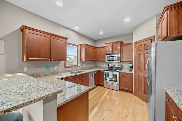 kitchen featuring light stone countertops, appliances with stainless steel finishes, light hardwood / wood-style floors, a kitchen bar, and kitchen peninsula