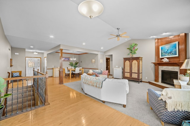 living room featuring lofted ceiling, a large fireplace, light wood-type flooring, and ceiling fan