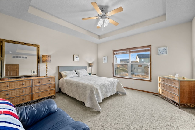 carpeted bedroom featuring a raised ceiling, ceiling fan, and a textured ceiling