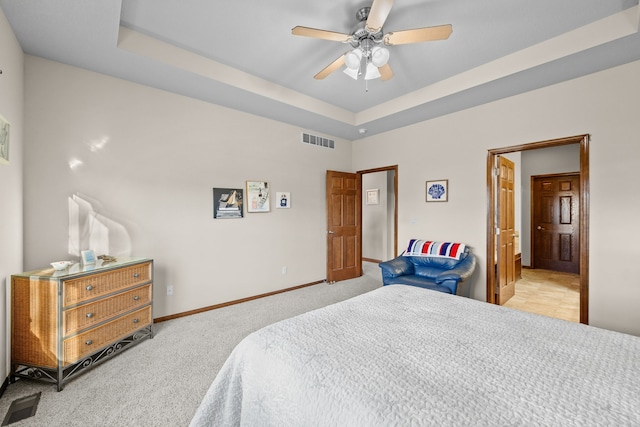 carpeted bedroom featuring a tray ceiling and ceiling fan