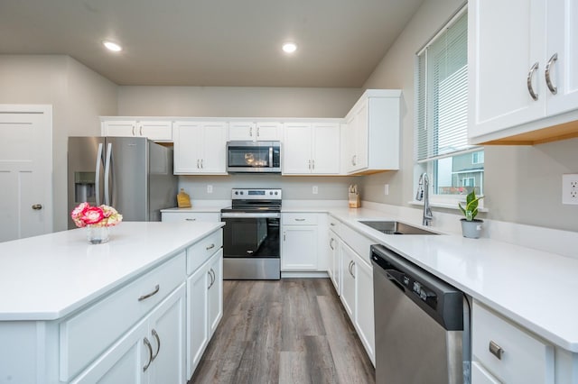 kitchen with appliances with stainless steel finishes, sink, hardwood / wood-style flooring, white cabinets, and a center island