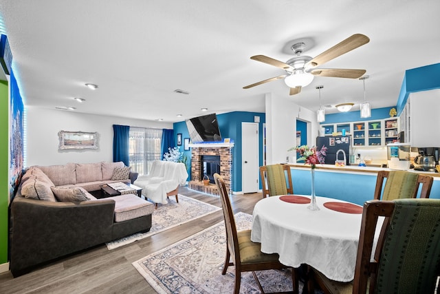 dining area featuring ceiling fan, a fireplace, and light hardwood / wood-style flooring