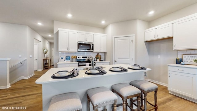 kitchen with light wood-type flooring, appliances with stainless steel finishes, white cabinetry, and a center island with sink