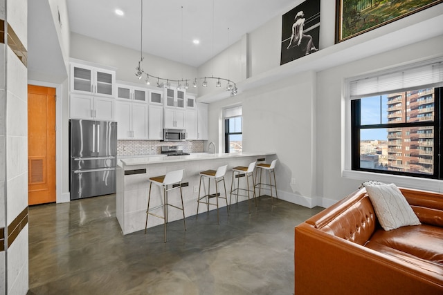 kitchen featuring white cabinets, a kitchen breakfast bar, a towering ceiling, appliances with stainless steel finishes, and tasteful backsplash