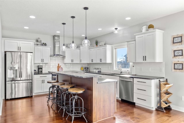 kitchen featuring a center island, wall chimney range hood, hanging light fixtures, dark hardwood / wood-style flooring, and stainless steel appliances