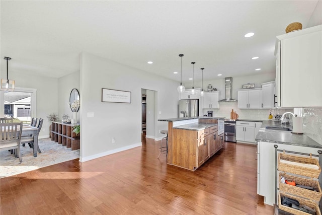 kitchen with appliances with stainless steel finishes, wall chimney exhaust hood, decorative light fixtures, hardwood / wood-style floors, and a kitchen island