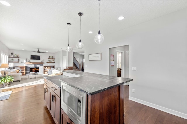 kitchen featuring ceiling fan, wood-type flooring, pendant lighting, a center island, and stainless steel microwave