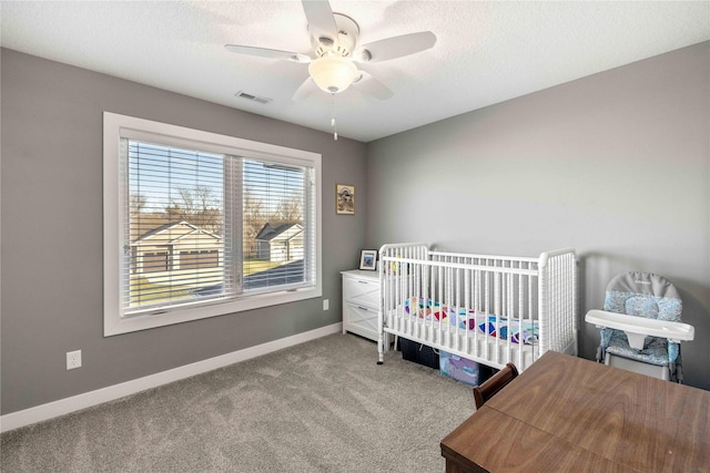 carpeted bedroom featuring ceiling fan, a nursery area, and a textured ceiling