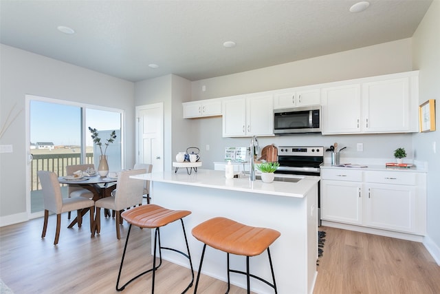 kitchen with a kitchen bar, appliances with stainless steel finishes, white cabinetry, and an island with sink