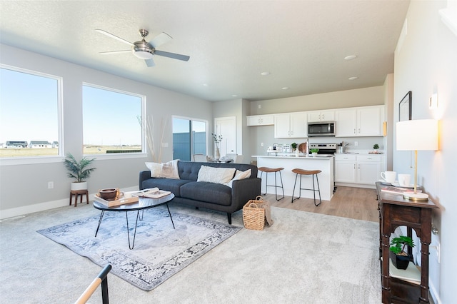 living room featuring ceiling fan, light hardwood / wood-style flooring, and a textured ceiling