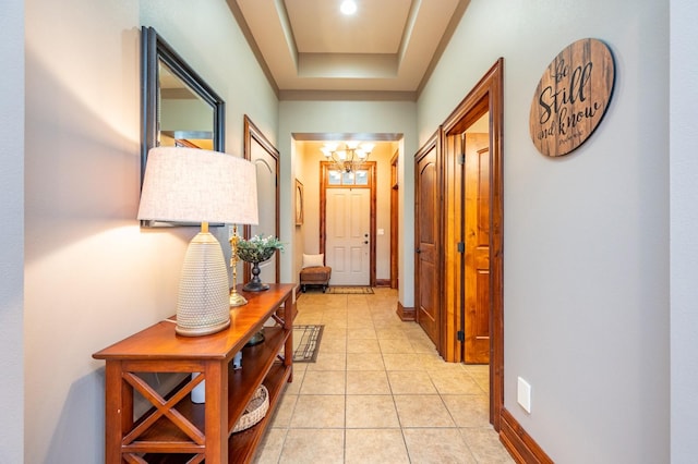 hallway with light tile patterned floors, a raised ceiling, and a notable chandelier