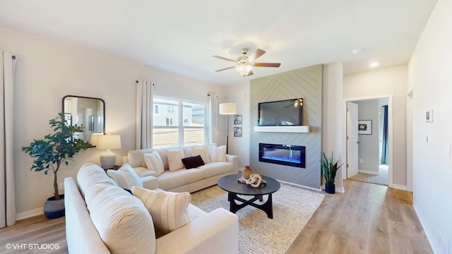 living room with light wood-type flooring, a large fireplace, and ceiling fan