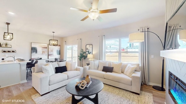 living room with ceiling fan with notable chandelier, light hardwood / wood-style floors, and sink