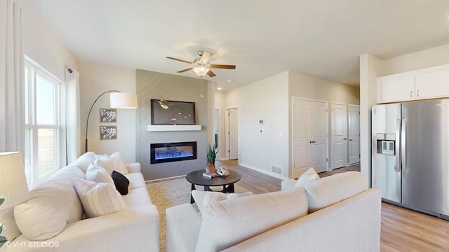 living room with light wood-type flooring, a large fireplace, and ceiling fan