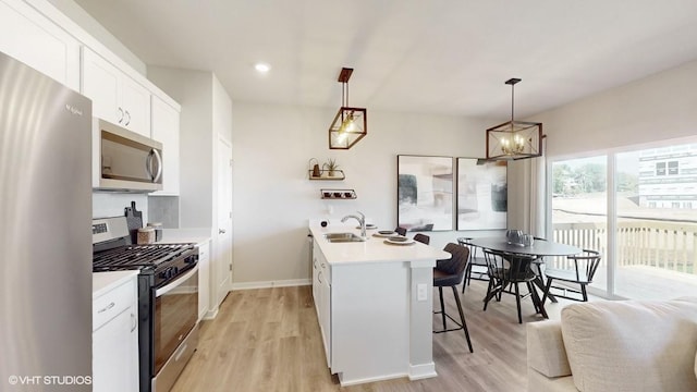 kitchen with hanging light fixtures, white cabinets, stainless steel appliances, and light hardwood / wood-style floors