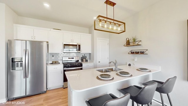 kitchen featuring white cabinets, hanging light fixtures, light wood-type flooring, kitchen peninsula, and stainless steel appliances