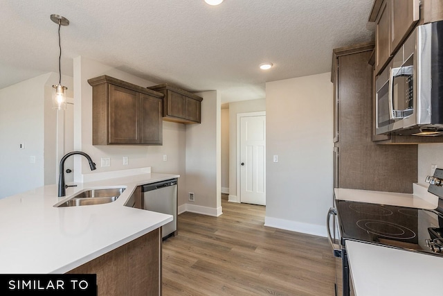 kitchen with dark brown cabinetry, sink, hardwood / wood-style floors, pendant lighting, and appliances with stainless steel finishes