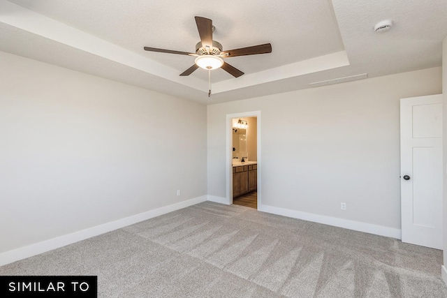 unfurnished room with a raised ceiling, ceiling fan, light colored carpet, and a textured ceiling