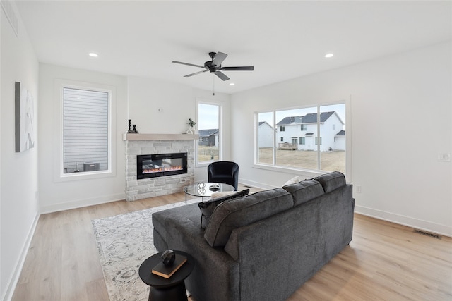 living room featuring ceiling fan, a stone fireplace, and light wood-type flooring