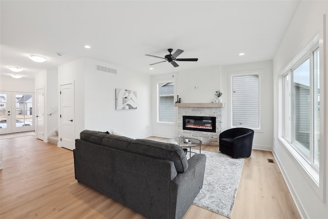 living room featuring a stone fireplace, light hardwood / wood-style floors, french doors, and ceiling fan