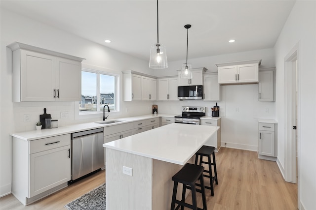 kitchen with sink, a breakfast bar, stainless steel appliances, a kitchen island, and light wood-type flooring