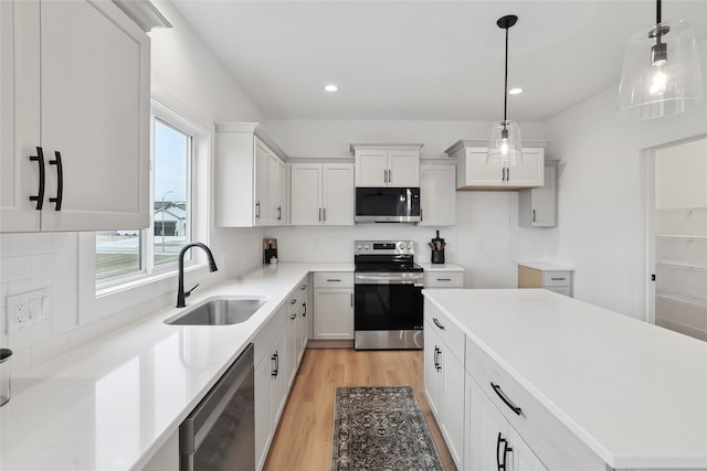 kitchen featuring sink, white cabinetry, hanging light fixtures, stainless steel appliances, and light wood-type flooring