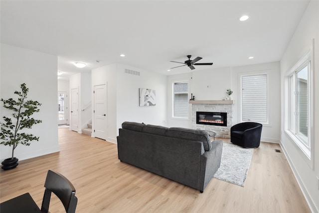 living room with ceiling fan, plenty of natural light, a fireplace, and light wood-type flooring