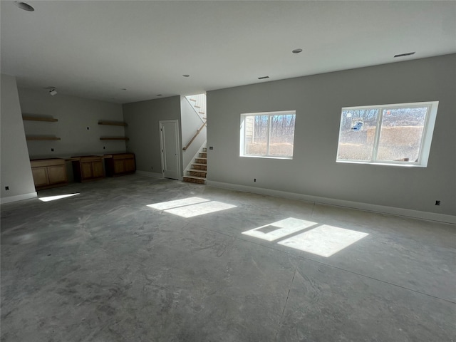 unfurnished living room with stairway, baseboards, and unfinished concrete floors