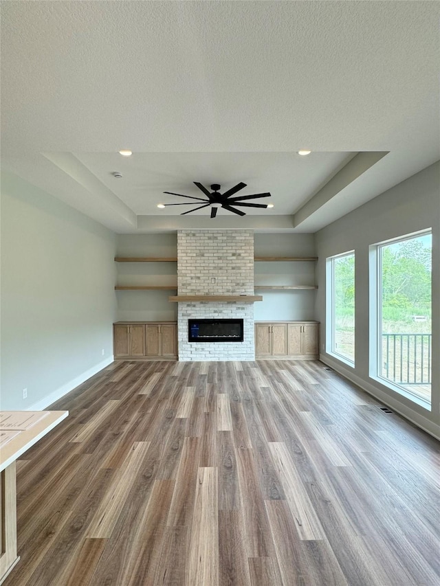 203 Hudson Ave, Van Meter, IA 50261 - unfurnished living room with a tray ceiling, wood finished floors, baseboards, ceiling fan, and a fireplace