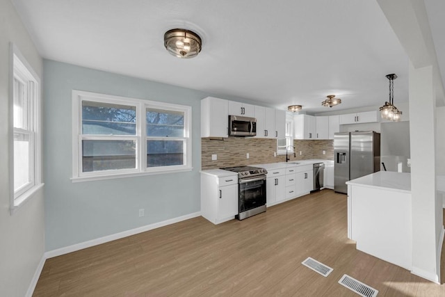 kitchen featuring decorative backsplash, appliances with stainless steel finishes, decorative light fixtures, light hardwood / wood-style flooring, and white cabinets