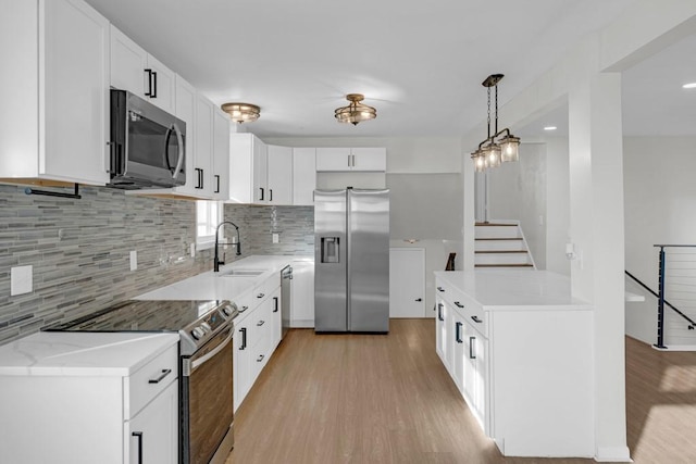 kitchen with sink, light hardwood / wood-style floors, pendant lighting, white cabinets, and appliances with stainless steel finishes